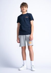 Marineblauwe katoenen T-shirt met korte mouwen en een klein oranje tekstontwerp, gecombineerd met grijze shorts met oranje branding en witte sneakers.