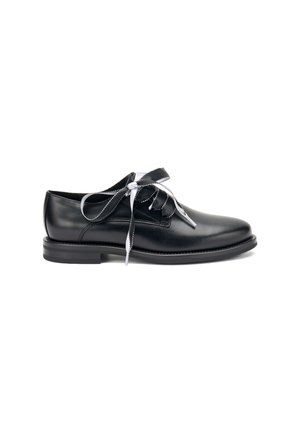Zapato de vestir de cuero negro con puntera redonda, suela plana y cordones decorativos blancos. Presenta una textura suave y detalles de costura mínimos.