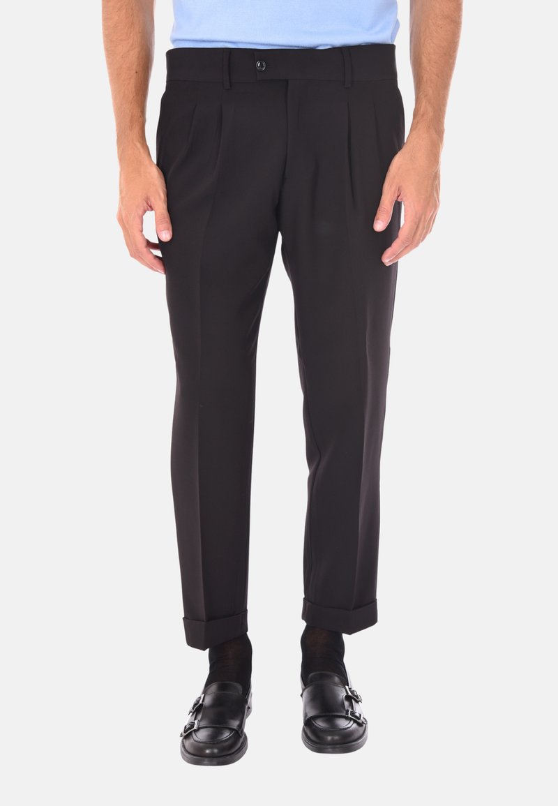 Pantaloni neri su misura con gamba dritta, dotati di pieghe frontali e risvolti. Indossati con una camicia azzurra chiara e mocassini neri.