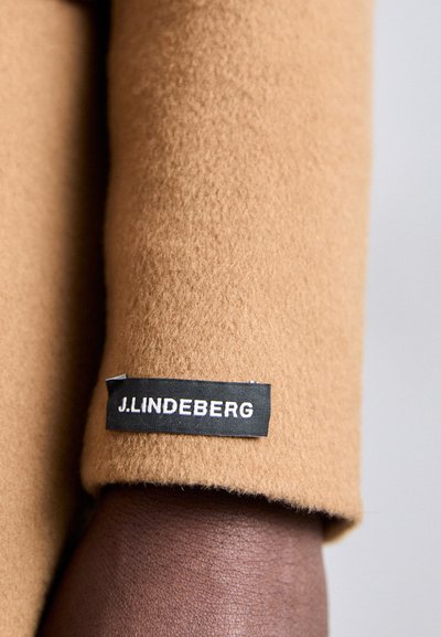 Kamelenwol stof met een zachte textuur en een manchet mouw. Bevat een zwart label met witte tekst, "J.LINDEBERG."