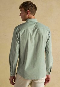 Zeleno-biely pruhovaný dlhý rukáv s golierom na zapínanie, so zaobleným spodným okrajom a manžetami na gombíky. Hladká textúra látky.