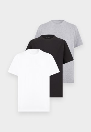 Trois t-shirts unis à manches courtes avec col rond en blanc, noir et gris, empilés sur un fond gris clair.