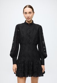 Black lace dress with a high collar, button front, and long puff sleeves. Features a flared hem with ruffled accents and intricate floral patterns.