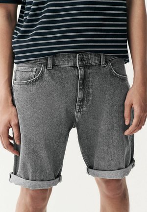 Grå denimshorts med oprevet kant, der har en frontlomme og knaplukning, båret med en navy- og hvidstribet skjorte.