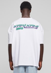Balta didelė t-shirt su trumpomis rankovėmis, ant nugaros puikuojasi spalvingas grafikos logotipas: "KARL KANI 1989" žalia ir purpurine spalvomis.