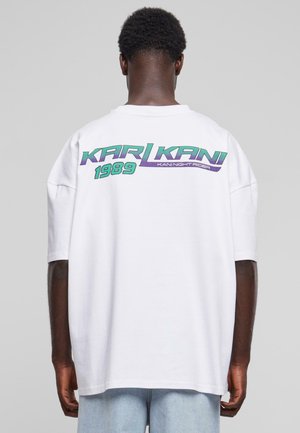 Hvid oversized t-shirt med korte ærmer, som har et farverigt grafisk logo på ryggen: "KARL KANI 1989" i grøn og lilla.