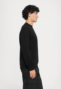 Sweatshirt preto com um decote redondo, mangas longas e punhos canelados, apresentando um design simples e descontraído. Textura suave, detalhe mínimo.