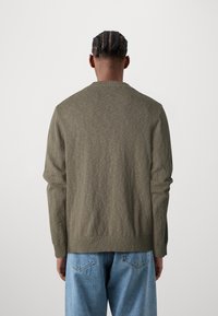 Suéter de punto verde olivo con cuello redondo, dobladillo y puños acanalados, combinado con jeans de mezclilla azul claro, mostrando una tela texturizada.