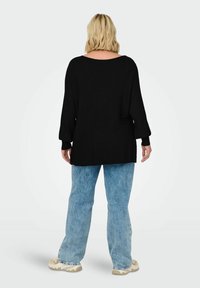 Black, ribbed knit oversized sweater with wide sleeves, paired with light blue, slightly distressed jeans and cream sneakers.