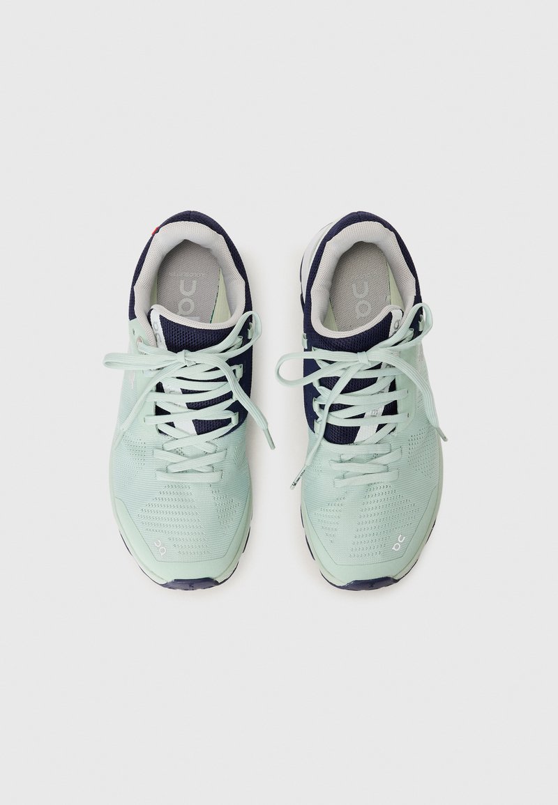 Hellgrüne Sportschuhe mit Mesh-Oberfläche, marineblauen Akzenten, runder Zehenpartie und flachen Schnürsenkeln. Logo an der Seite und gepolsterter Innenbereich.
