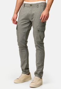 Pantalones cargo de tela gris claro con un acabado texturizado, que cuentan con bolsillos laterales y un diseño ceñido. Combinados con zapatillas beige.