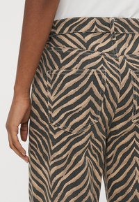 Džinsu bikses ar zebras printu, gaiši brūnā un melnā krāsā, ar aizmugures kabatām, vidēji paceltu vidukli un reljefa apdari.