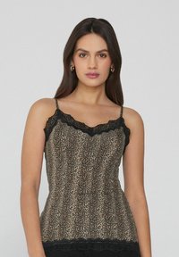 Camisole s leopardím potiskem, který má černé krajkové detaily podél výstřihu a lemu, nastavitelné ramínka a přiléhavý střih.