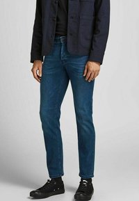 Dark blue denim jeans, slim fit, mid-rise, with five pockets, subtle whiskering detail, paired with black lace-up sneakers.