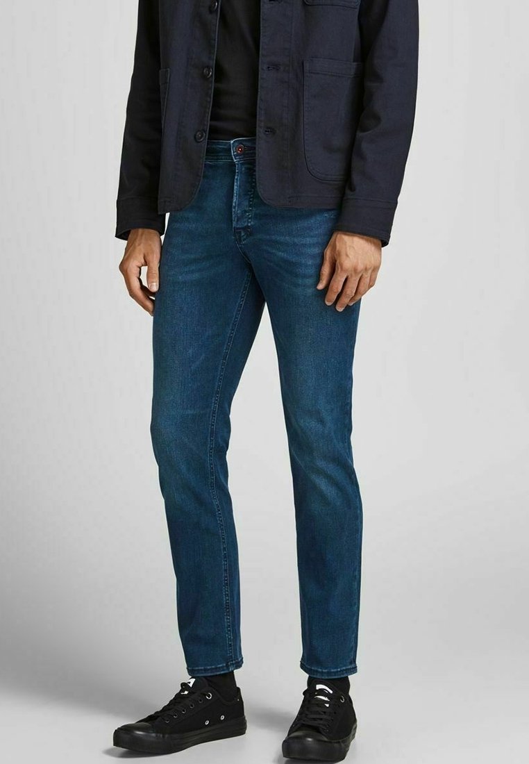 Dark blue denim jeans, slim fit, mid-rise, with five pockets, subtle whiskering detail, paired with black lace-up sneakers.