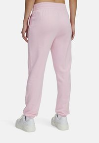 Roze trainingsbroek met een rekbare tailleband, taps toelopende pijpen en zijzakken. De stof lijkt zacht met een gladde textuur. Gekleed met witte sneakers.