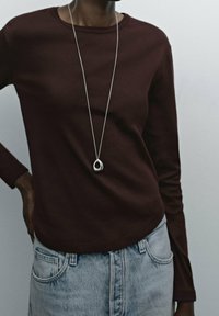 Burgundy long-sleeve shirt in a soft fabric, paired with light blue high-waisted denim shorts. Features a layered silver pendant necklace.