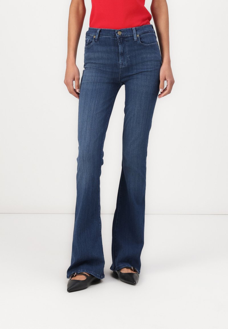 Blugi evazați de culoare albastru închis, cu talie medie, confecționați din denim. Dispun de un design clasic cu cinci buzunare și închidere frontală cu nasture.