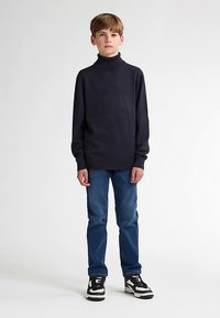Dunkelblauer Rollkragenpullover aus weichem Stoff, kombiniert mit blauen Jeans und schwarz-weißen Sneakers, mit lockerer Passform und langen Ärmeln.