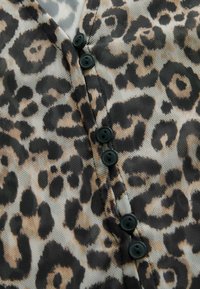 Bluzica s leopard uzorkom koja sadrži crne gumbe, laganu mrežastu tkaninu i kombinaciju smeđih i crnih uzoraka na površini.