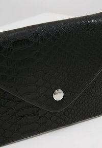 Pochette enveloppe en cuir noir à texture de crocodile avec une fermeture à bouton pression circulaire argenté.