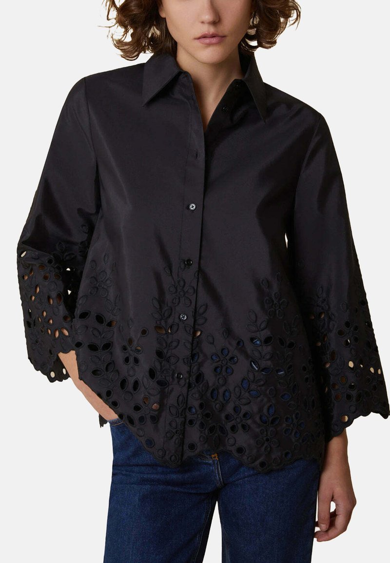 Camicia nera in cotone con colletto, caratterizzata da maniche svasate e intricati motivi floreali intagliati lungo l'orlo. Chiusura frontale con bottoni.