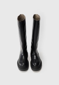 Botas de cuero negras hasta la rodilla con puntera redondeada y suela gruesa; textura suave y diseño minimalista.