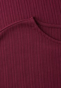 Primer plano de tela burdeos acanalada con detalle de costura curvada visible sobre textura tejida y suave.