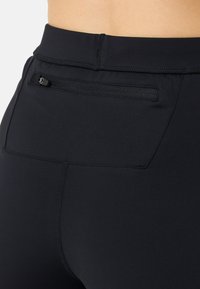 I leggings sportivi neri presentano un alto punto vita, una texture liscia e una piccola tasca con zip sulla parte posteriore per riporre oggetti.