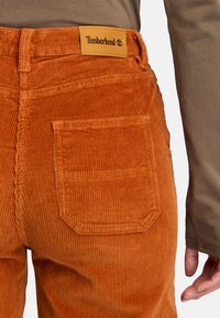 Katoenen corduroy broek in stralend oranje met ribbeltextuur. Voorzien van een bruine leren Timberland-logo patch en details op de achterzak.