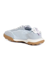 Zapatilla deportiva azul claro que combina texturas lisas y de ante, suela de goma, cordones blancos y una etiqueta trasera con detalles en morado.