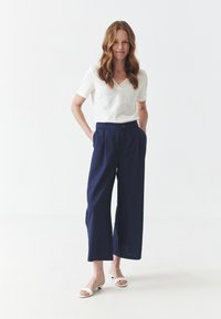 Top blanco de manga corta con escote texturizado, combinado con pantalones anchos de color marino y sandalias blancas. Diseño simple, tejido ligero.