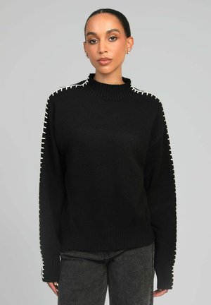 Pull noir en tricot avec un col haut, présentant des coutures blanches le long des épaules et des manches pour un contraste. Coupe décontractée.