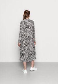 Robe fleurie avec un fond noir, ornée de fleurs blanches et roses. Manches longues, longueur midi et portée avec des baskets blanches.