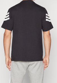 Černé bavlněné tričko s třemi bílými pruhy na každém rameni, krátkými rukávy, kulatým výstřihem a klasickým střihem.