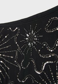 Black fabric with silver sequins arranged in floral and starburst patterns for decorative embellishment.