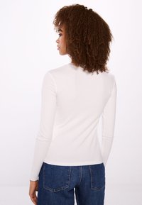 Langslavige, fitted T-shirt in licht crème, van een katoenmix. Glad textuur met een ronde halslijn, gecombineerd met hoog in de taille gesneden blauwe jeans.