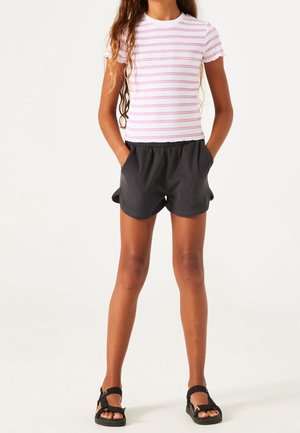 Witte kortemouwen shirt met roze strepen, gecombineerd met zwarte elastische shorts. Heeft een losse pasvorm en wordt gedragen met zwarte sandalen.