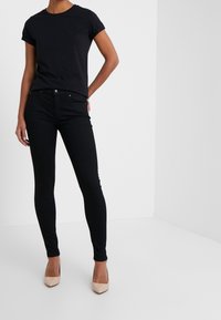 T-shirt en coton noir avec des manches roulées, associé à un jean skinny noir. Escarpins à bout pointu beiges. Design simple et ajusté.