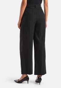 Černé široké kalhoty vyroben�é z hladké, lehké látky. Vysoký pas s kapsami na zadní straně. Nosené s černými lakovanými lodičkami.