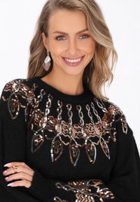 Maglione nero con scollo rotondo, caratterizzato da dettagli intricati in paillettes bronzo e argento. Texture morbida con maniche ampie.