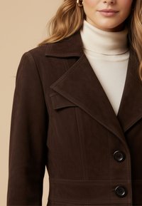 Brown suede jacket with a notched collar, two buttons, and a defined waist. Worn over a light turtleneck sweater.