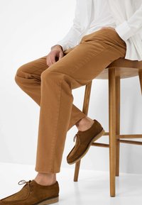 Pantaloni di cotone beige a vestibilità slim, con tasche laterali e una leggera consistenza. Abbinati a scarpe in scamosciato marroni con lacci e suole in gomma.