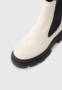 Krémová kožená Chelsea bota s černými elastickými bočními panely a silnou černou robustní podrážkou.