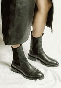 Black leather ankle boots with elastic side panels, rounded toes, and textured rubber soles, paired with a black leather skirt.