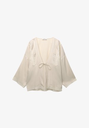 Helle beige Bluse im Kimono-Stil mit weiten Ärmeln, einem tiefen V-Ausschnitt und filigranem Spitzendetail an den Schultern und dem Saum. Mit Bindebändern in der Taille.
