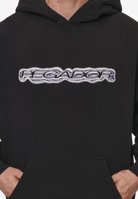 Sweat à capuche noir arborant un logo "PEGADOR" brodé en violet et blanc bien en évidence sur la poitrine. Le matériau semble doux avec une poche avant.