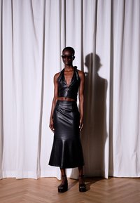 Top cropped de couro preto e saia evasê, com uma textura suave e design minimalista. Sapatos de plataforma pretos robustos e óculos de sol redondos completam o visual.