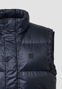 Marineblauer Steppwesten mit hohem Kragen, Druckknöpfen, gestepptem Design und einem kleinen schwarzen Logopatch auf der Vorderseite. Leicht und isoliert.
