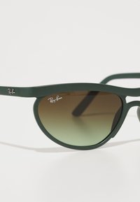 Ochelari de soare din plastic verde cu lentile degradate maro. Dispune de un design elegant și logo-ul Ray-Ban pe rame.